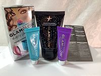 Photo of GlamGlow skincare set items including the GalacticCleanse cleanser tube, ThirstyMud and GravityMud treatment tubes, and the product packaging box with artistic face design.