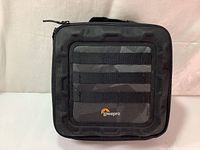 Front view of the black Lowepro Drone Guard CS 200 bag showing the Lowepro logo on front zippered pocket with horizontal elastic loops.