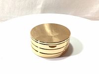 Closed shiny gold three-tiered round compact case.