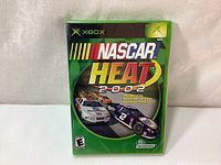 Front cover of the NASCAR Heat 2002 Xbox game showing original sealed packaging with racing car artwork and Xbox branding.