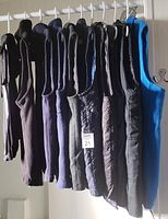 Ten men's vests hanging on a rack showing various styles and dark colors with one bright blue fleece vest.