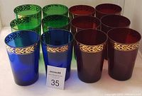 Full set of twelve Egyptian water drinking glasses arranged in three groups of four, green, red and blue colors visible, each featuring ornate gold trim near the rim.