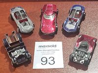 Five vintage Hot Wheels Redline toy cars arranged around auction card, showing vehicle variety and condition