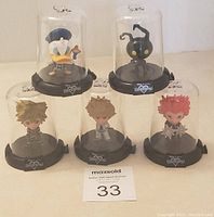 Five Kingdom Hearts character figures under clear domes on black bases including Donald Duck, Heartless, Sora, Roxas, and Axel.