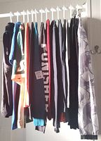 Photo showing 12 assorted men's long sleeve tops and shirts hanging, including hoodies and casual tops in various colors such as navy, turquoise, orange, red, black and beige.