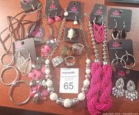Full overview of 18 brand-new Paparazzi jewelry pieces including necklaces, earrings, and rings on a wooden surface.