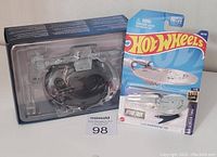Photo of Promellian Battle Cruiser model in protective plastic casing and blue display box branded with Star Trek logo, alongside Hot Wheels NCC-1701 spaceship still in packaging.