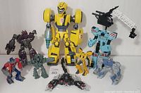 Full lot of seven Transformer action figures of various sizes and colors on white background.