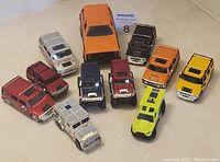 Overview of 11 toy trucks including multiple Hummer models in red, maroon, blue, orange, yellow, silver, and neon green.