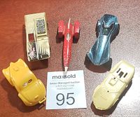 Five vintage toy cars arranged on a wooden surface, photo shows top view to display shape and details including a yellow coupe, a metallic gold car with exposed engine, a red race car, a metallic blue streamlined car, and a pale yellow coupe.