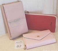 Photo of three women's wallets: pink wrist wallet, red zip-around wallet, and peach envelope wallet.