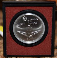 Front side of the 1976 Montreal Olympics $5 silver coin featuring a diver and the Olympic logo, displayed in a case with red velvet lining.
