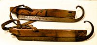 Side view of two antique wooden ice skates with curved metal blades and leather straps.