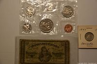 Six Canadian coins sealed in clear plastic with Queens Elizabeth II on some coins, accompanied by an old Dominion of Canada banknote and a Canadian coin in 1941 holder.