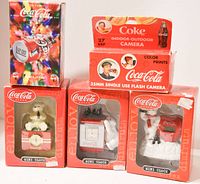 Image showing five assorted Coca-Cola collectibles in original packaging including three mini clocks, one 35mm single-use flash camera, and one clock radio.