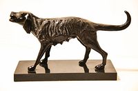 Side view of the bronze hunting dog sculpture on rectangular black marble base showing dog's texture and posture.