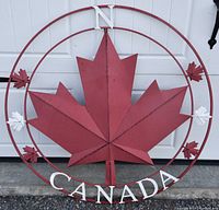 Front view of the large metal Canada decorative sign showing the front of the red maple leaf and white CANADA text with compass points
