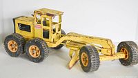 Side angled view of the heavily used yellow Tonka grader toy showing metal body with paint wear and rubber wheels.