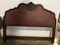Full frontal view of carved wood and brown upholstered headboard with nail head trim.