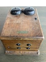 Top view of the antique wooden telephone box with two black metal bells and small switch, showing surface wear and hardware.