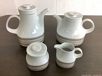 Photo showing all four ceramic pieces in set: two teapots (one taller, one shorter), creamer, and sugar bowl arranged on a tabletop. Clear view of design and condition.