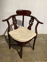 Front view of the corner chair showing the curved armrests, marble seat with cushion, and carved wooden details on backrest.
