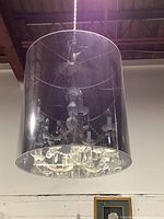 Full view of crystal chandelier with oversized clear cylinder shade hanging from ceiling.