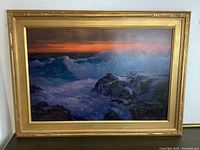 Frontal view of the signed original seascape painting in its ornate gold frame against a white wall.