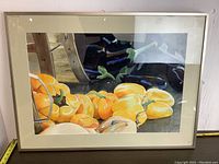 Framed watercolor painting of a still life showing yellow bell peppers and eggplants with vibrant colors, signed by artist McKinnon. Visible crack on the glass in the upper right corner and wear on the frame edges.