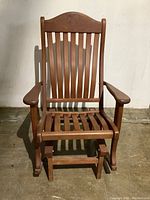 Front view of solid wood glider rocking chair showing slatted seat and backrest with curved top and armrests.