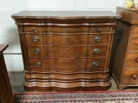 Front view of solid wood chest of drawers showing curved front and metal oval handles on four drawers.