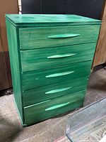 Side angled view of green wooden dresser showing five horizontal drawers and integrated handles.