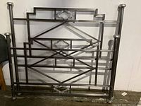 Full view of the hand forged metal headboard with geometric design and rounded finials on posts.