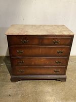 Front view of solid wood chest with marble top and four drawers against wall.