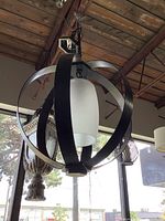 Modern chandelier with metal orb bands around a frosted glass central shade seen hanging indoors against a ceiling and window background.