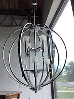 Front view of the chrome spherical dining room chandelier showing curved chrome bands and five frosted glass light shades.