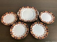 Set of five Royal Albert side plates with floral and gold decorative border shown from above on a table, one square with handles and four round.