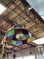 View of Tiffany style stained glass light fixture suspended from ceiling, showing multicolor glass segments and chain.