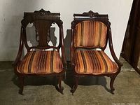 Two vintage occasional chairs made of solid wood with curved arms, carved wooden details, and striped velvet upholstery on seat and backrest.