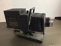Side view of vintage projector showing bellows, lens, and base.
