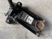 3 ton hydraulic floor jack showing label, lifting saddle, handle socket, signs of rust and dirt