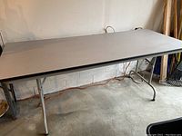 Side view of six-foot folding table with gray Formica top against wall showing metal legs and underside structure