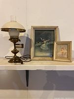 Desk lamp, large and small framed ballet prints on shelf against white wall.