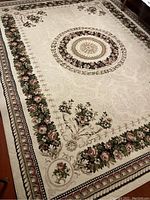 Full view of the 8x10 floral area rug showing the cream background with multicolored floral border and central medallion.