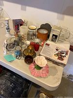 Variation of vintage candleholders, glassware including shot glasses, mini frames, and a box of silverware, arranged on a white table showing condition and variety.