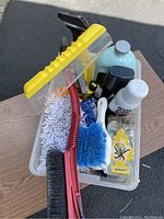 White plastic bin containing multiple car cleaning brushes, various detergent bottles, an air freshener, and rags shown from top down.