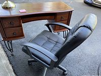 Side view of wood computer desk showing wrought iron legs and black faux leather office chair next to it