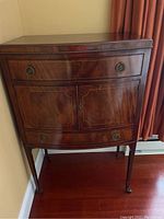 Front view of a curved front mahogany cabinet with two drawers and a double door cabinet below, standing on four legs with wheels, placed in a corner.
