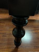 Close-up of black turned wood coffee table leg on hardwood floor.