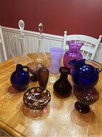 Wide view of entire glassware collection showing vases, pitchers, candy dishes, and vessels in various shades of blue, purple, and clear glass.
